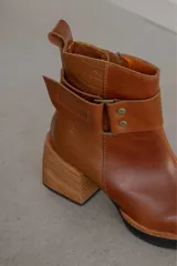 Bota corta de cuero marrón con puntera redondeada y taco cuadrado. Presenta una correa con hebilla alrededor del tobillo y cierre lateral.