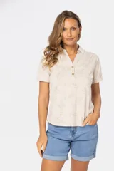 Camisa beige con estampado floral, de manga corta y cuello camisero con botones.