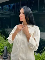 Camisa color off-white con detalles calados en forma de flores en los hombros y cuello. Tiene cierre frontal con botones a presión y cordón decorativo.