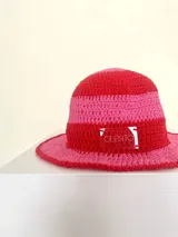 Sombrero tipo bucket tejido a crochet a mano, con hilo 100% algodón y diseño a rayas en tonos rosa y rojo. Presenta una etiqueta con el logo de la marca Cilento en el frente.