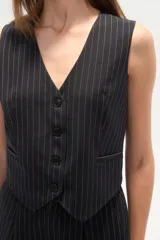 Chaleco de vestir sin mangas, color negro con finas rayas verticales blancas. Presenta escote en V, cierre frontal con botones y bolsillos falsos a la altura de la cintura.