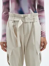 Pantalón color beige claro, de corte holgado, con bolsillos laterales y cinturón con hebilla metálica.