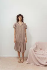 Vestido color beige con botones frontales, cuello camisero, mangas cortas abullonadas y falda con volantes.