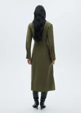 Vestido camisero midi color verde oliva, con cuello camisero, mangas largas con puños abotonados, cierre frontal con botones, cinturón con hebilla forrada y abertura lateral en el bajo.