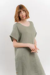 Vestido corto color verde oliva, confeccionado en lino, con corte recto y mangas cortas. Presenta bolsillos laterales y botones decorativos en los laterales.