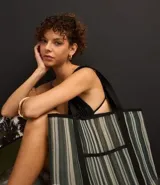 Bolso de playa rectangular de poliéster con rayas verticales en tonos de verde, gris y blanco. Tiene asas de algodón negras y un bolsillo externo.