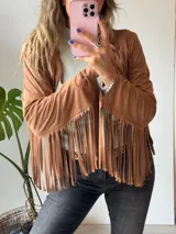 Chaqueta marrón de gamuza sintética con flecos en mangas y ruedo.