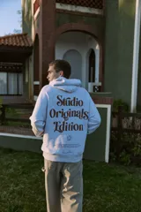 Canguro gris melange con capucha, mangas largas y estampado en la espalda con la inscripción "Studio Originals Edition" en color marrón.