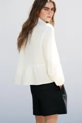 Camisa color crudo confeccionada con lino, de corte recto, cuello solapa con escote pico y manga larga. Presenta aplicación de pasamanería en el frente y cierre frontal con botones forrados a tono.