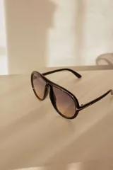 Lentes de sol estilo aviador con marco negro de policarbonato y lentes degradados de violeta a amarillo.