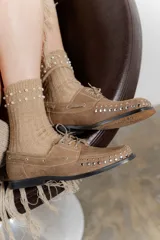 Mocasín de cuero color marrón con tachas metálicas plateadas en la puntera y laterales.