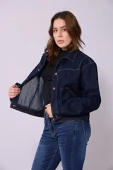 Campera de jean de color azul oscuro, con corte cropped y costuras en contraste color caramelo. Presenta cuello clásico, cierre frontal con botones metálicos y bolsillos a la altura del pecho y laterales.