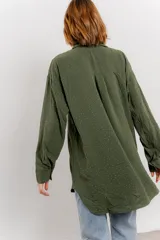 Camisa verde militar con estampado de lunares blancos, de corte oversize, con cuello camisero, cierre frontal con botones y bolsillo en el pecho.