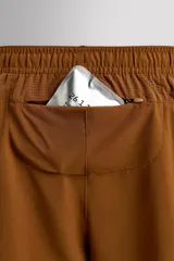 Pantalón corto deportivo color marrón oliva, con cintura elástica ajustable con cordón, bolsillos frontales y bolsillo trasero con cierre. Presenta forro interior y detalle de logo estampado en la pernera.