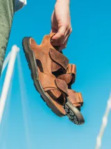 Sandalias de cuero color marrón con tiras ajustables con velcro y suela de goma negra.