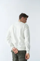 Buzo de felpa color crudo, de corte recto, con cuello redondo, puños y ruedo acanalados.