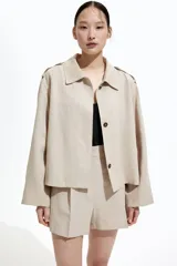 Chaqueta corta color beige, de corte oversized, con cuello clásico, charreteras abotonadas, bolsillos laterales y trabilla con botón en los puños.