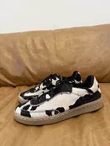 Zapatillas bajas con estampado de vaca en blanco y negro, con cordones negros y suela color caramelo.