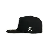 Gorro negro de visera plana con logo de Hellstar bordado en blanco en el frente. El diseño incluye una estrella, un rostro y llamas.