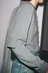 Chaqueta de punto color rosa pálido, con cuello redondo y cierre frontal de botones oscuros. Presenta mangas largas y un corte a la cintura.