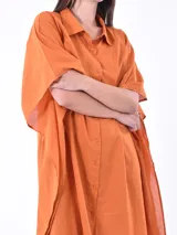 Vestido camisero color naranja de corte holgado, con cuello camisero, mangas cortas tipo kimono y cierre frontal con botones.