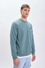 Sudadera verde con cuello redondo y mangas largas. Estampado en la espalda con la frase "Scorpions thrive", un escorpión, el número 073 y un texto descriptivo.