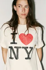 Remera color crudo de corte holgado con mangas cortas y cuello redondo. Estampado frontal con el texto "I ❤️ NY" en color negro y rojo.