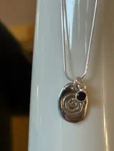 Collar con cadena plateada y dije redondo plateado con diseño de espiral.