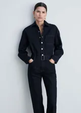Mono largo de denim azul oscuro, con cuello camisero, mangas largas con puños abotonados, trabillas, cinturón con hebilla metálica, cierre frontal con botones a presión y cuatro bolsillos.