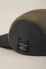 Gorra de cinco paneles color verde militar, con panel frontal color beige, panel trasero color gris oscuro y visera negra.