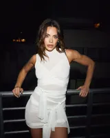 Mini vestido blanco ajustado al cuerpo, con cuello alto y mangas cortas. El diseño se caracteriza por múltiples tiras de tela que se envuelven y anudan alrededor del torso y la cintura.