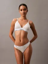 Conjunto Calvin Klein de ropa interior, compuesto por un corpiño triangular con elástico con logo y una colaless con elástico con logo. Diseño a rayas verticales en tonos beige y blanco.