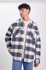 Sobrecamisa de franela a cuadros azul marino, gris y blanco, con cuello clásico, cierre frontal con botones, dos bolsillos de parche en el pecho y mangas largas con puños abotonados.