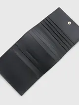Billetera plegable con acabado granulado, cierre de botón a presión y múltiples ranuras para tarjetas, destacando el monograma de Tommy Hilfiger.