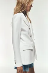 Blazer color blanco hueso, de corte entallado y doble botonadura dorada. Tiene cuello con solapa, mangas largas con hombreras y bolsillos delanteros con solapa.