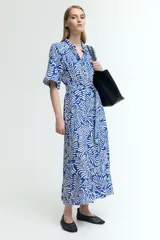 Vestido midi camisero con estampado de hojas blancas sobre fondo azul. Tiene cuello camisero, botonadura frontal, mangas cortas raglán, elástico en la cintura y cinturón extraíble para atar.