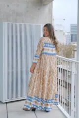 Vestido largo color beige con estampado abstracto en tonos marrones y azules, con cuello mao, mangas largas con puños elásticos y cierre frontal con botones.