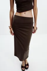 Falda midi color crema, de tiro alto con cintura elástica y detalle de pliegues laterales.