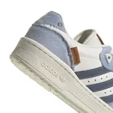 Zapatillas urbanas Adidas Rivalry Low, color blanco con detalles en celeste y azul marino. Confeccionadas en cuero y gamuza, con las tres tiras características de la marca en los laterales.