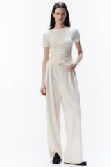 Pantalón sastre color crema de punto crepé con pinzas, tiro alto, cintura elástica, cinturón decorativo con hebilla de metal y piernas amplias rectas.