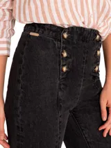Pantalón de jean negro con corte boot leg, tiro alto y cierre frontal con botones dorados.