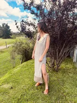 Vestido largo de lino color beige con cuello redondo, sin mangas, abertura lateral y terminación con flecos. Presenta detalle de cuero en el escote.