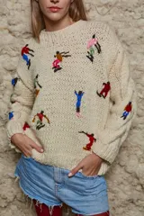 Sweater de lana color crema, tejido a mano con cuello redondo y mangas largas con trenzas. Presenta bordados de figuras esquiando.