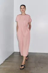 Vestido midi color marrón confeccionado en hilatura con mezcla de algodón y lino. Tiene cuello redondo, manga corta caída y detalle de pliegues en la cintura. Cierre en la espalda con abertura y botón.