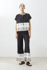 Blusa de manga corta con cuello redondo y cierre frontal parcial con botones. Presenta un diseño tie dye en tonos grises y blancos en la parte inferior.