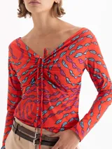 Top de punto color rojo con estampado de labios en azul y fucsia. Presenta escote en V profundo con jareta ajustable para anudar, mangas largas y calce al cuerpo.