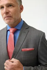 Ambo de vestir gris con saco de dos botones, solapa de muesca, dos bolsillos con solapa y un bolsillo de ojal en el pecho. Pantalón de vestir a juego, de corte recto.
