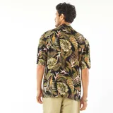 Camisa de manga corta con estampado de hojas tropicales en tonos verdes, marrones y rosados sobre fondo negro.
