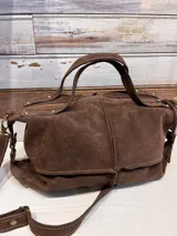 Bolso bandolera marrón de gamuza, con doble asa corta y correa larga regulable.