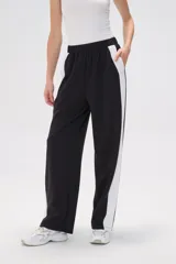 Pantalón de jogging negro con cintura elástica, corte holgado y una franja vertical blanca a lo largo de la pierna.